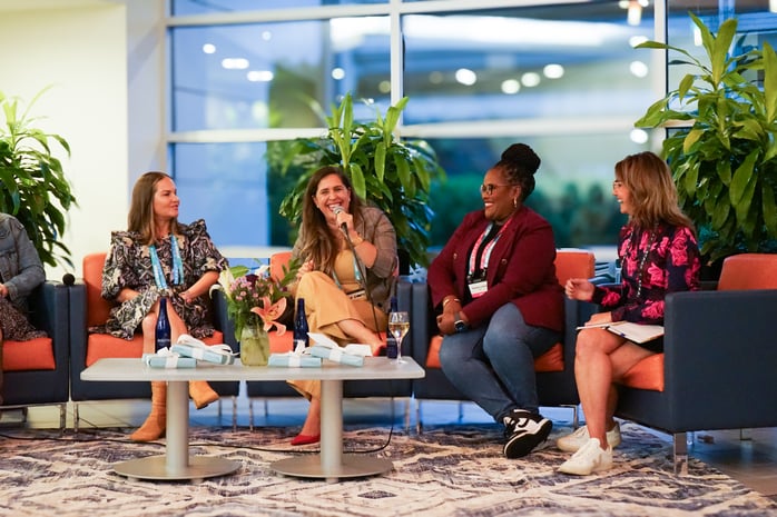 Diverse group of women professionals laugh at a panel discussion about their experiences as women in the working world